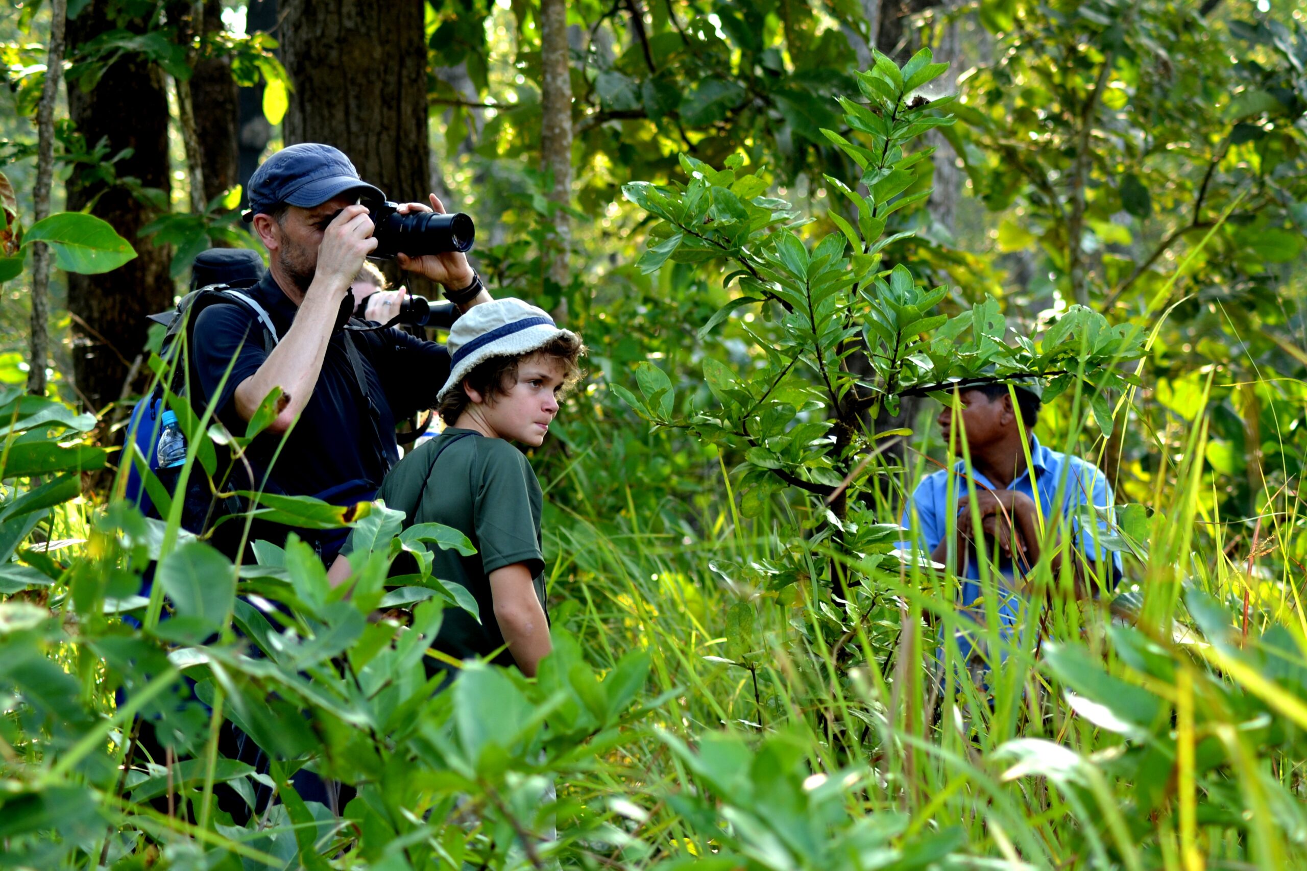Wildlife photographer with telephoto lens and local guide observing animals in dense Chitwan National Park jungle during safari from Rhino Lodge & Hotel Sauraha Nepa
