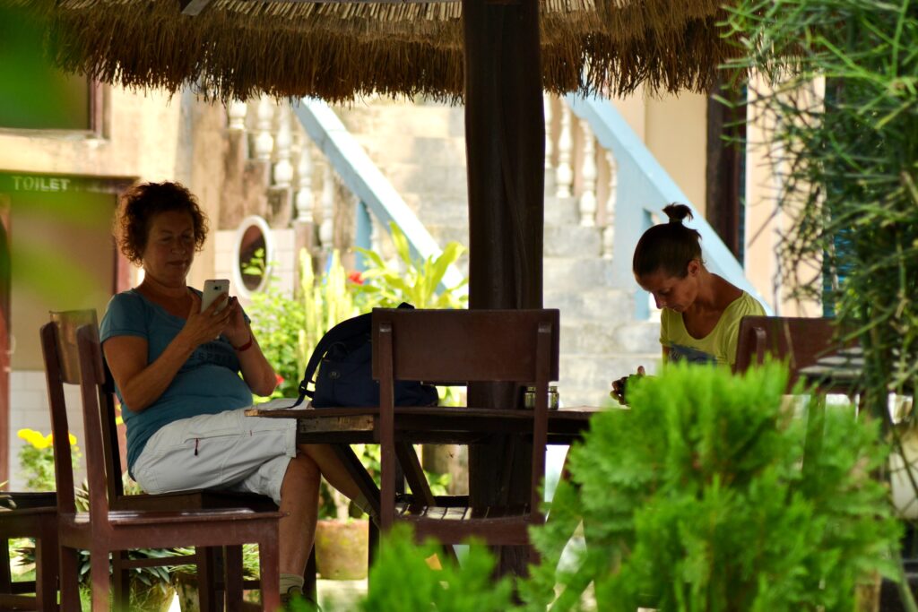 Two women relaxing at thatched-roof outdoor seating area surrounded by tropical plants at Rhino Lodge & Hotel Sauraha Chitwan Nepal