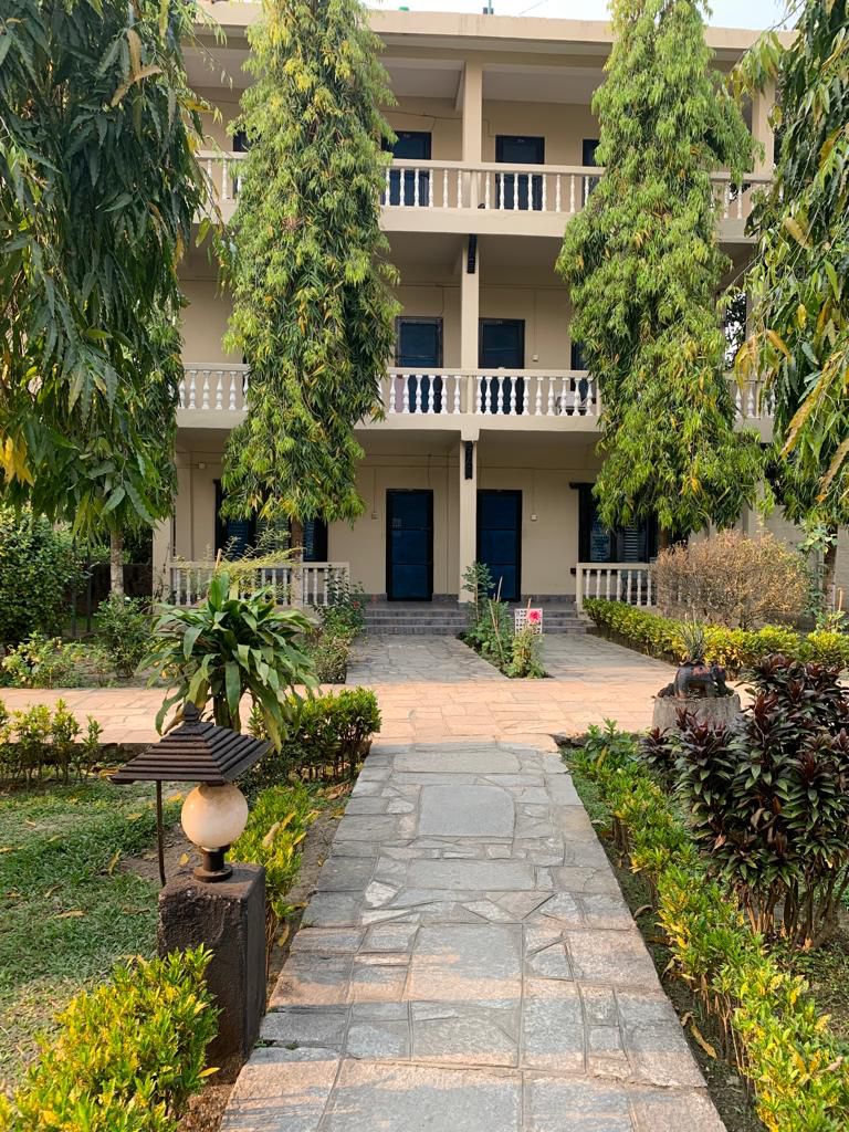 Three-story hotel building with private balconies and stone pathway through tropical garden at Rhino Lodge & Hotel Sauraha Chitwan Nepal